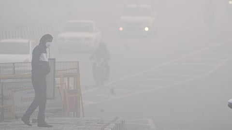 A man crosses a road amid dense fog in New Delhi.