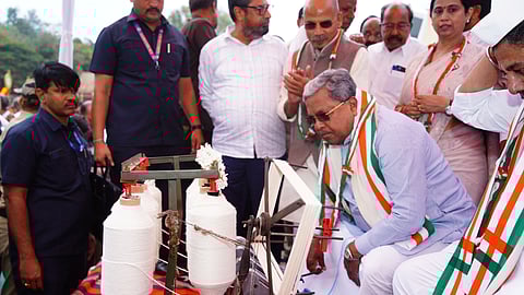 CM Siddaramaiah tries to spin cotton threads with a traditional wood spinner.