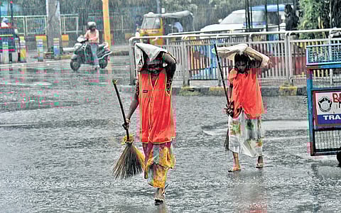 GHMC workers cover their heads with plastic cover to shield themselves from rains in Hyderabad on Thursday