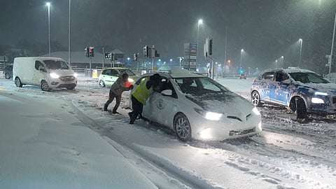 People help to push cars stuck in snow in Leeds, England, Sunday.