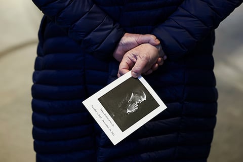 A mourner carries a picture of former President Jimmy Carter as she stands near his casket as he lies in repose at the Jimmy Carter Presidential Library and Museum in Atlanta, Monday, Jan. 6, 2025.