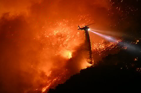 A fire fighting helicopter drops water as the Palisades fire grows near the Mandeville Canyon neighborhood and Encino, California, on January 11, 2025.