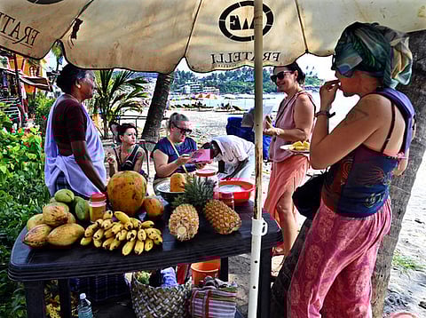 Standalone photo:International tourists enjoying fresh cut-fruits from a wayside fruit stall at Kovalam beach.