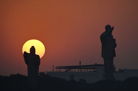 Silhouettes at Sunset: A serene view of Buddha and Dr B R Ambedkar statues framed against a glowing orange sky as the sun sets in Hyderabad.