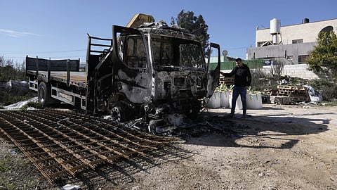 A Palestinian stands beside a trick that was torched in an attack by suspected Israeli settlers in the West Bank village of Jinsafut, Tuesday, Jan. 21, 2025.