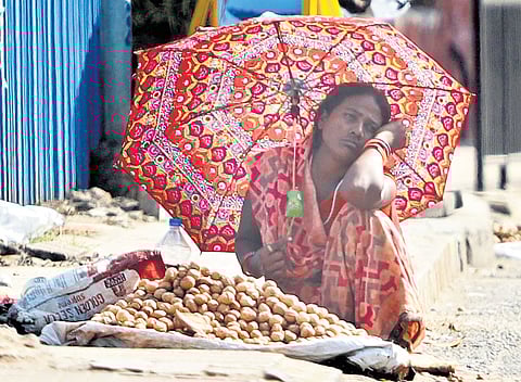 A street vendor waits for customers while covering herself from the scorching sun with an umbrella in Hyderabad on Wednesday.