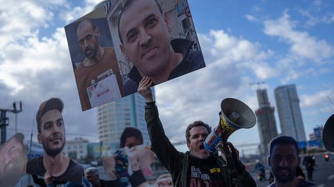 A demonstrator holding photos of freed Israeli hostage Eli Sharabi before and after his captivity blocks a highway during a protest demanding all hostages release from Hamas captivity, in Tel Aviv, Israel.