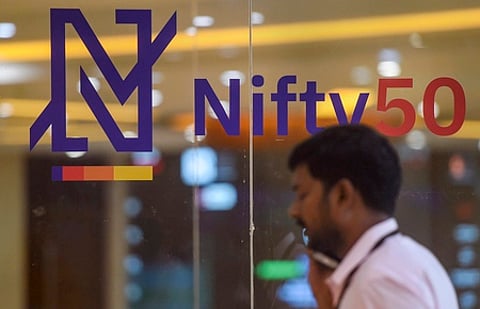 A man talks on phone at the National Stock Exchange as its new logo for for the benchmark Nifty50 is seen on a glass-wall, in Mumbai.