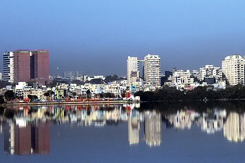 Urban skyline reflecting on a calm Hussainsagar lake under a clear blue sky in Hyderabad