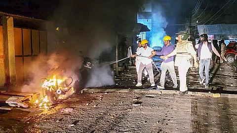 Police personnel try to douse a fire after clashes that broke out during a rally celebrating the Indian team's victory over New Zealand in the Champions Trophy final, in Mhow, Madhya Pradesh, Sunday, March 9, 2025.