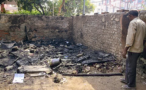 A man looks at the charred remains at the site after a fire gutted a makeshift tent near the AGCR Enclave at Anand Vihar, in New Delhi, Tuesday, March 11, 2025.