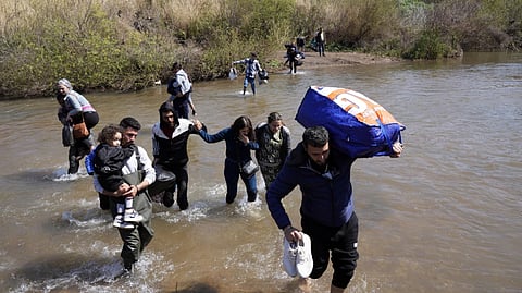 In this photo from March 11, 2025, Syrian families who fled the clashes in Syria hold their luggage as they cross a river marking the border between Syria and northern Lebanon near the village of Heker al-Daher in Akkar province, Lebanon.