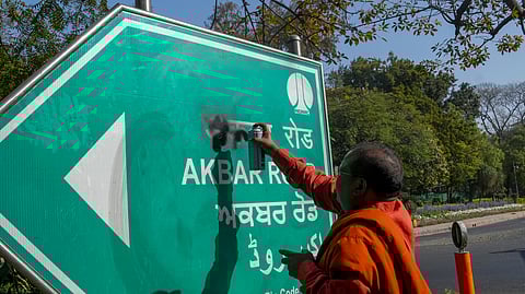 A protestor defaces the signboard of 'Akbar Road' demanding that the road be renamed after Maharishi Valmiki, in New Delhi.
