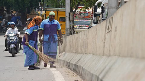 Civic workers seen cleaing the road during the sunny weather at Outer ring road in Bengaluru.