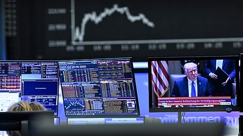 Behind a television monitor showing US President Donald Trump, the display board with the Dax curve shows falling share prices in Frankfurt, Germany, on Thursday, April 3, 2025, after the tariff package announced by Trump pushed share prices sharply into negative territory.