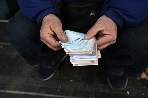 A street money exchanger poses for a photo without showing his face as he counts Iranian banknotes at a commercial district in downtown Tehran, Iran, Dec. 23, 2022.