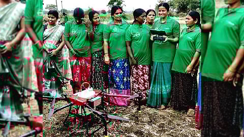 Women agricultural labourers are seen using drones to spray pesticides.
