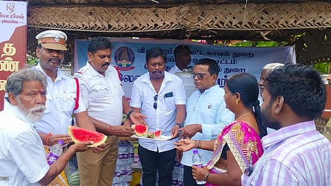 The stall features a shaded canopy, water dispensers, and containers filled with sliced watermelon and chilled buttermilk.