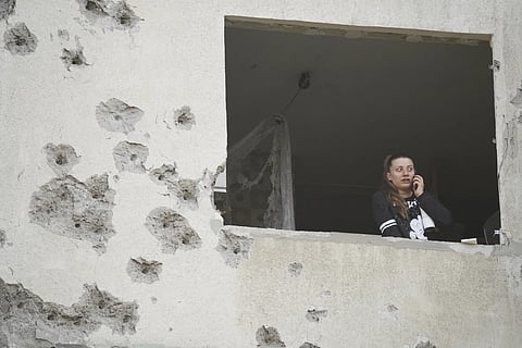A woman looks through the window of her damaged apartment following a Russian strike in Kharkiv, Ukraine, Friday, April 18, 2025.