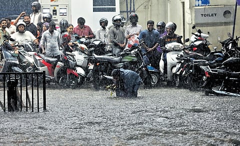 A man tries to clear the blockage at a manhole as commuters
wait for the very heavy rain that lashed Hyderabad on Friday to
subside.