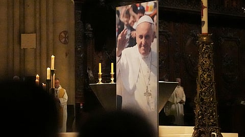 People attend a ceremony inside Notre Dame cathedral where a poster shows Pope Francis following the Vatican's announcement of his death, Monday, April 21, 2025 in Paris.