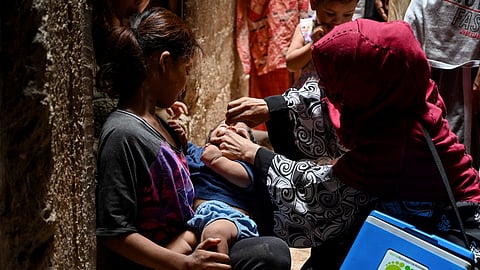 A health worker (R) administers polio vaccine drops to a child during a polio vaccination campaign in Pakistan