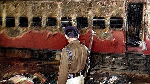 A policeman looks over a burnt coach and belongings of people at Godhra station, on 28 February 2002, some 200 km from Ahmadabad.