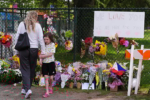Visitors stand near a growing memorial the day after a driver killed multiple people during a Filipino community festival Sunday, April 27, 2025, in Vancouver, British Columbia.
