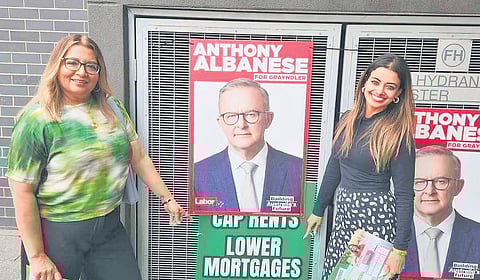 Hannah Thomas (right) along with another Greens candidate posing near the photograph of her rival and Prime Minister Anthony Albanese