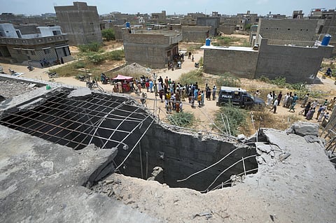 A big hole is seen on a rooftop of a house suspected to have been damaged in Indian drone attack as residents, behind, gather near a cordoned off site, where Pakistan's air defense system shot down a suspected Indian drone in Karachi, Pakistan, Thursday, May 8, 2025.