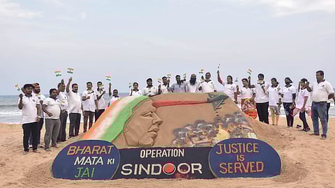 People wave the Indian tricolours as they stand next to a sand art by artist Sudarsan Pattnaik in tribute to the Indian armed forces after the Operation Sindoor, at the beach in Puri