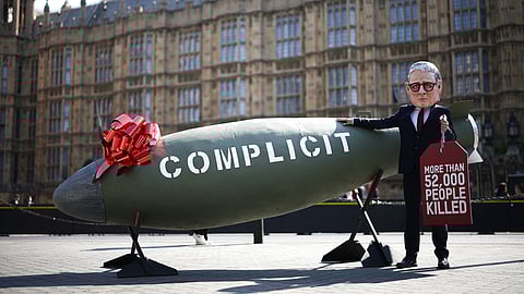 A protestor dressed as Britain's Prime Minister Keir Starmer poses in front of a 16-foot replica of an MK-84 2,000-pound bomb labelled with the word "Complicity" and with a tag reading "more than 52,000 people killed", referring to the number of people killed in Gaza by Israel, in front of the Palace of Westminster, home of the Houses of Parliament, in central London, on May 12, 2025.