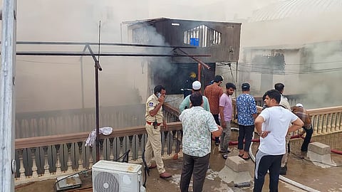 A police official and others stand as smoke billows from a building after a fire broke out, in Hyderabad, Telangana, Sunday, May 18, 2025. A blaze triggered by a suspected short circuit in a building near the iconic Charminar on Sunday killed 17 people, including eight children, belonging to an extended family.