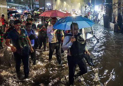 People holding umbrellas cross a road amid rain at Vashi in Mumbai,