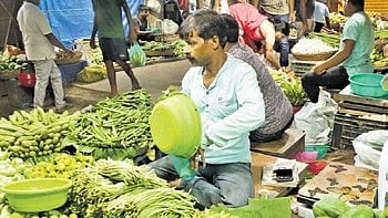 A vendor measuring and packaging produce for a customer at Unit-I vegetable market.