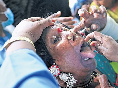 A volunteer attempts to open the mouth of a woman to administer the traditional ‘fish prasadam’