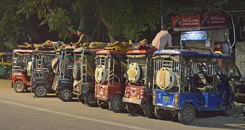 E-rickshaw drivers rest top of the their vehicles while charging them at a private charging station.