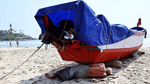 An elderly fisherman taking a nap on the shade of a fishing boat at the Kovalam in Thiruvananthapuram.