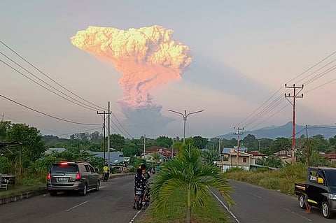 People watch as Mount Lewotobi Laki-Laki spews volcanic materials into the air during an eruption, in Maumere, Indonesia, Tuesday, June 17, 2025.