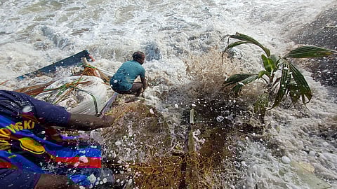 A fisherman is caught in the raging waves while trying to place sandbags to protect his house from sea erosion at Vettucaud.