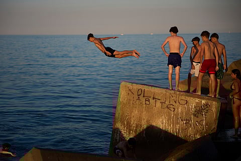 Young swimmers jump into the water from a rock on a breakwater on a hot day in Barcelona, Spain, Sunday, June 29, 2025.