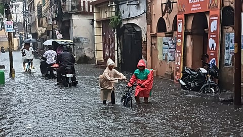 Two students wade through knee-deep waters on a road near Mahammadia Bazar square, after heavy rain lashes Cuttack on Tuesday.