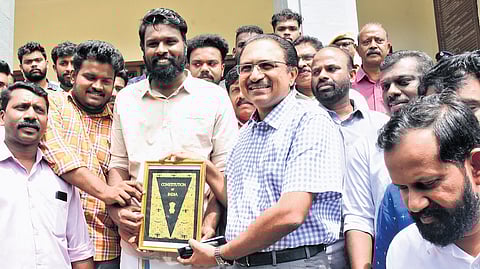 SFI workers present a copy of the Constitution to suspended Kerala University registrar K S Anil Kumar at the university headquarters on Thursday