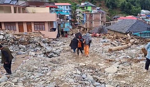 Locals carry their belongings as they walk amid the debris at a flood-affected area, at Thunag in Mandi district, Monday, July 7, 2025.