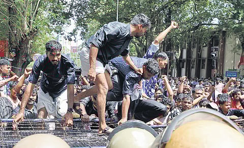 SFI activists scale the barricades erected by police in front of the Raj Bhavan during their protest against the alleged saffronisation of universities in Thiruvananthapuram on Thursday