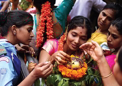 A woman lights the lamp on top of a bonam before offering prayers at Shri Ujjaini Mahakali Devasthanam Temple