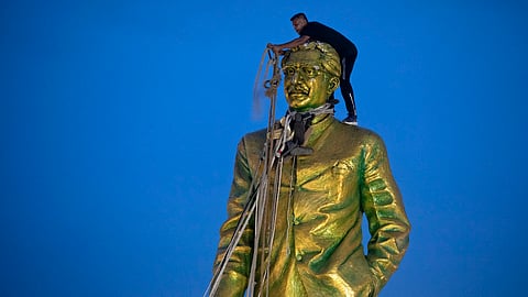 A man climbs to tie a rope around the head of a large statue of Sheikh Mujibur Rahman, father of Bangladesh leader Sheikh Hasina, as protesters try to bring it down after she resigned as Prime Minister, in Dhaka, Bangladesh, on Aug. 5, 2024.