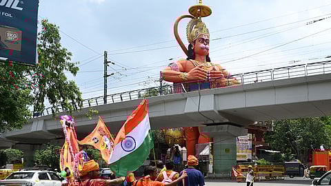 'Kanwariyas'', Lord Shiva devotees, walk past the statue of Lord Hanuman at Jhandewala area during the ongoing 'Kanwar Yatra'', in New Delhi.