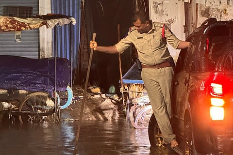 A cop stands on a car’s footrest as he clears a clogged manhole in Tolichowki after heavy rains on Wednesday