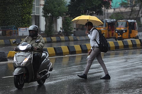 A man covers himself using an umbrella as he walks near Somajiguda Signal as light rain falls continuously in Hyderabad.